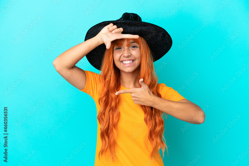 Young woman disguised as witch isolated on blue background focusing face. Framing symbol Young woman disguised as witch isolated on blue background focusing face. Framing symbol
