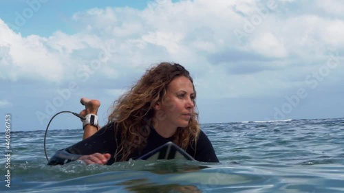 Video footage of surfer girl on white surf board in blue ocean pictured from the water in Bali