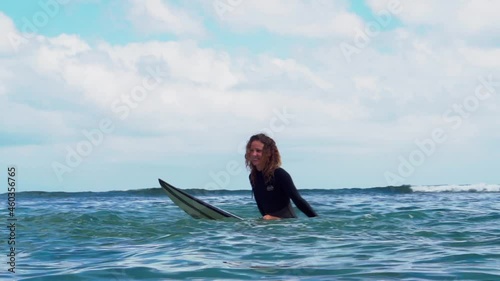 Video footage of surfer girl on white surf board in blue ocean pictured from the water in Bali