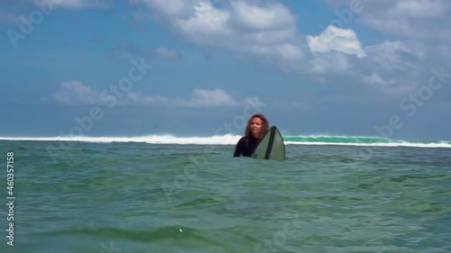 Video footage of surfer girl on white surf board in blue ocean pictured from the water in Bali