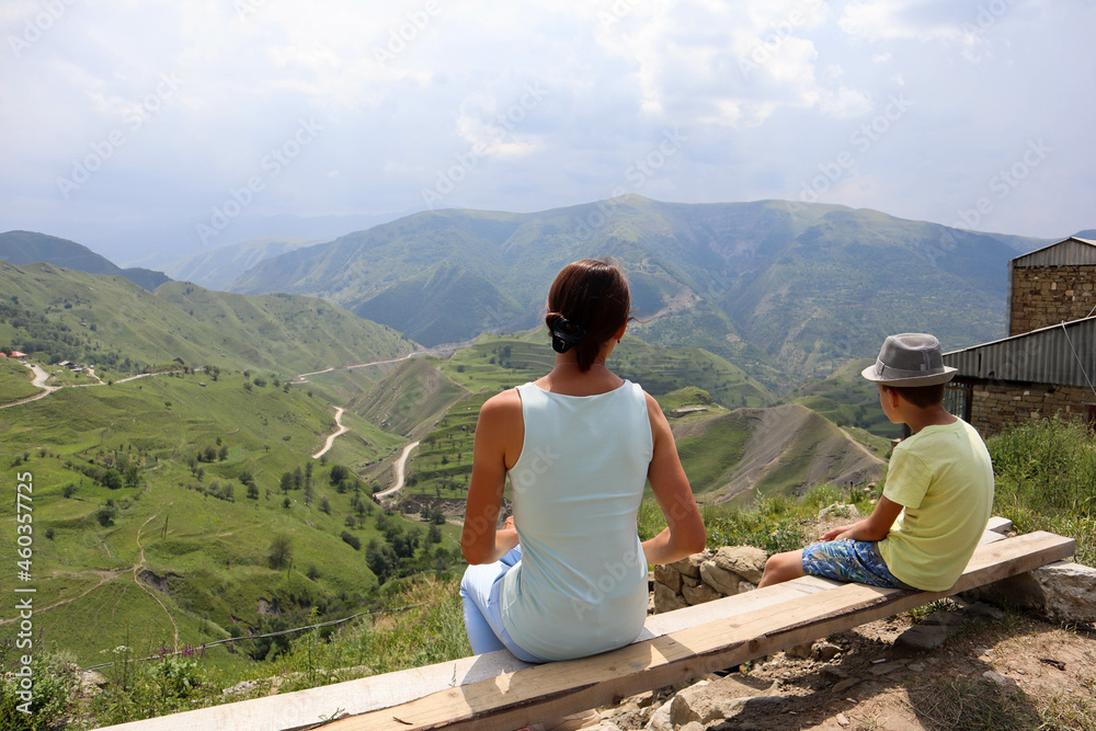 family mother and son sitting on a bench and enjoying amazing view to the valley in the mountains
