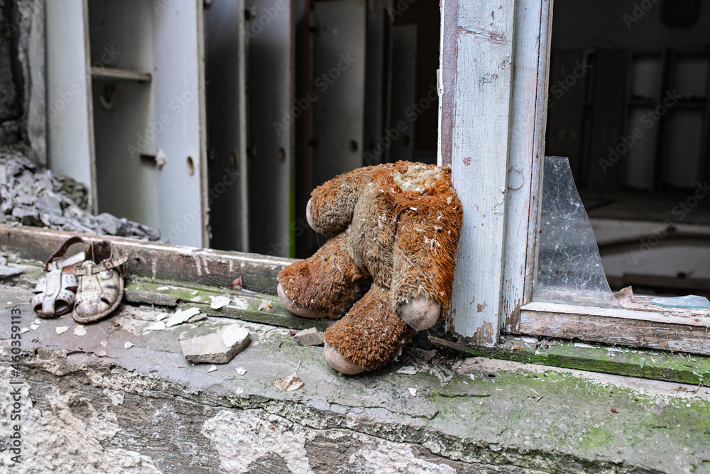 a headless teddy bear sits on a window sill in a ruined building