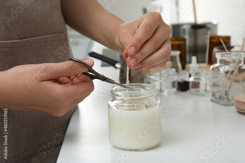 Woman cutting wick of homemade candle at table indoors, closeup