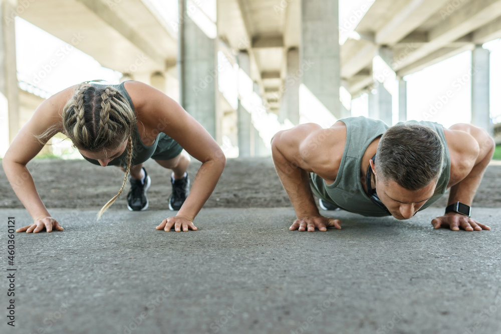 Athletic couple and fitness training outdoors. Man and woman doing push-ups exercise. - obrazy, fototapety, plakaty 