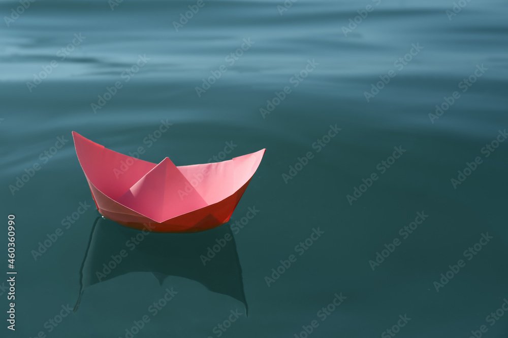 Pink paper boat floating on water surface, space for text