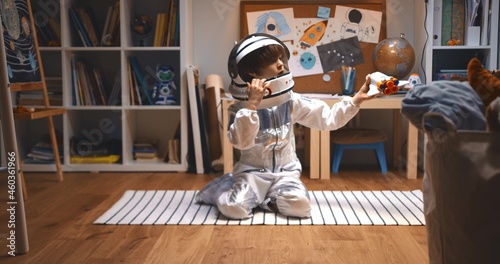 Childhood dreams about future. Happy little boy in astronaut suit playing space ship pilot, flying rocket toy on floor.
