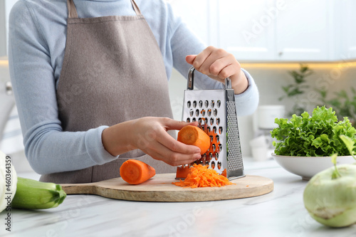 Photography Woman grating fresh ripe carrot at kitchen table, closeup