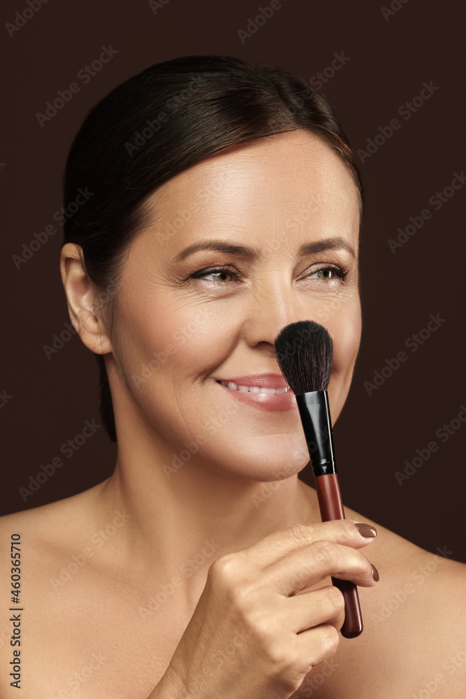 Beautiful middle aged woman with a makeup brush on brown background Beautiful middle aged woman with a makeup brush on brown background