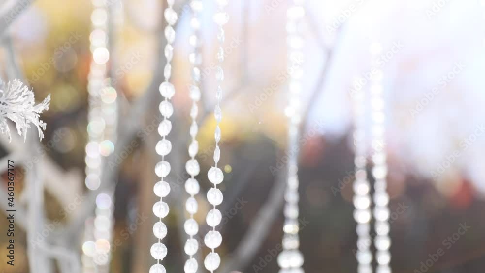 Glass, plastic, transparent beads in the form of crystals hang as decorations on the holiday close-up. White decor. Wedding ceremony on the street on the green lawn. Glass, plastic, transparent beads in the form of crystals hang as decorations on the holiday close-up. White decor. Wedding ceremony on the street on the green lawn.