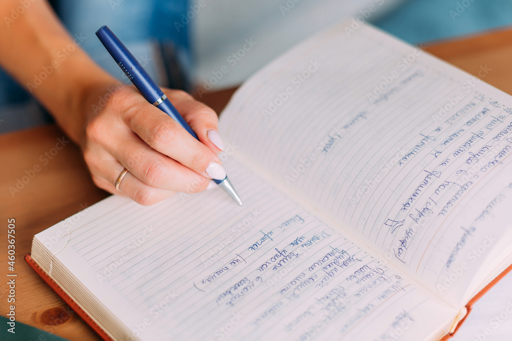 Woman writes down list of business or household chores in notebook. Close-up of hand, notebook and pen. Wedding ring is on a woman's hand. The handle is blue. There are a lot of notes in the notebook Woman writes down list of business or household chores in notebook. Close-up of hand, notebook and pen. Wedding ring is on a woman's hand. The handle is blue. There are a lot of notes in the notebook