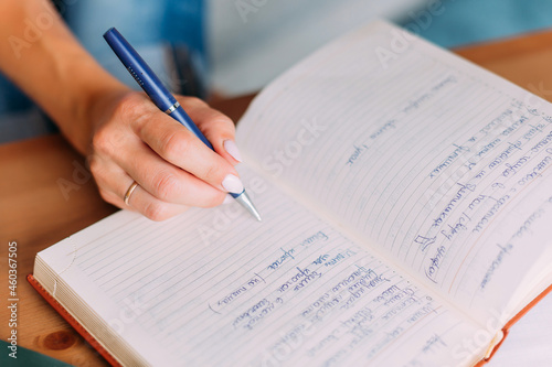 Woman writes down list of business or household chores in notebook. Close-up of hand, notebook and pen. Wedding ring is on a woman's hand. The handle is blue. There are a lot of notes in the notebook