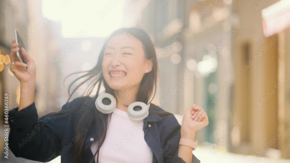 Portrait of happy asian girl enjoying success on mobile phone at city street. Closeup joyful young woman reading good news on phone in slow motion. . High quality 4k footage Portrait of happy asian girl enjoying success on mobile phone at city street. Closeup joyful young woman reading good news on phone in slow motion. . High quality 4k footage