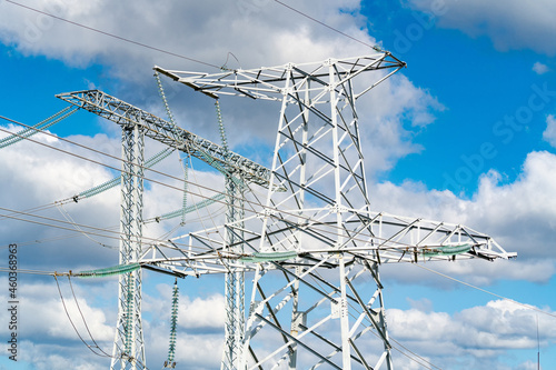 Electricity pylons and high-voltage power lines on the blue cloudy sky background. Power plant. Electrical power grid. View from below