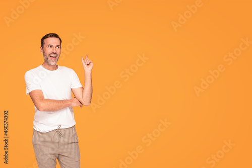 Handsome happy man smiling and looking at the camera, pointing with his finger at empty place, isolated on yellow studio background.