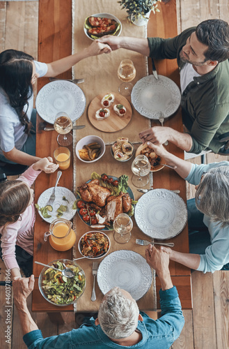 Top view of multi-generation family holding hands and praying while having dinner together