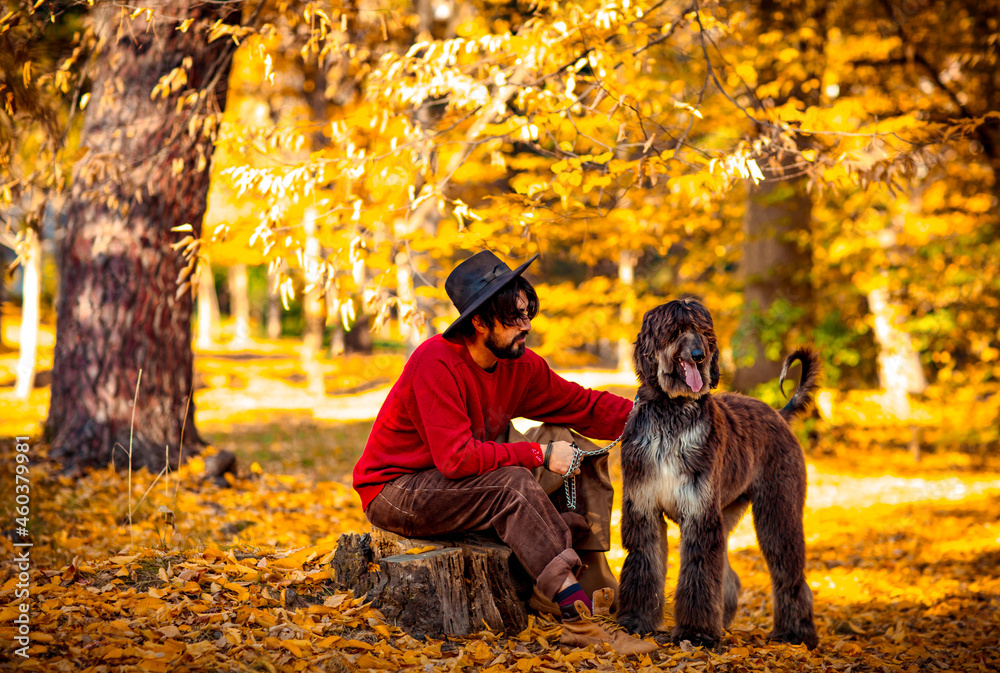 a handsome, brutal man in a red sweater and hat, walks in the park during the day, in autumn, with a large pedigreed dog a handsome, brutal man in a red sweater and hat, walks in the park during the day, in autumn, with a large pedigreed dog