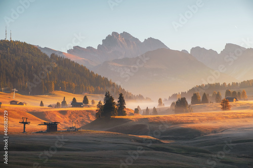 Alpe di Siusi (Seiser Alm) alpine meadow with beautiful foggy sunrise in the background with the Sassolungo and Langkofel mountains and Seceda mountain, South Tyrol