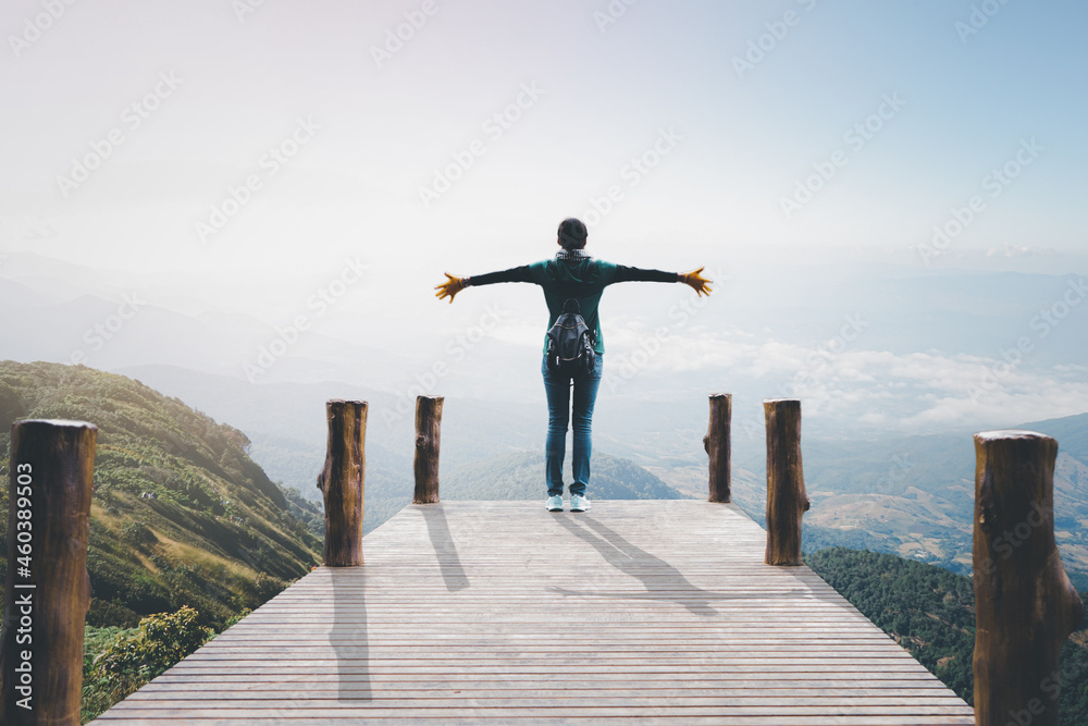 Asian woman standing with hands up achieving looking view sky. Girl welcomes a sun. Successful woman hiker open arms on a sunrise mountain top.