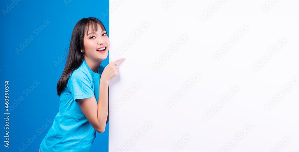 Banner, advertisement, sign board presentation concept. Excited surprise young woman pointing own finger on white placard empty copy space while standing over isolated blue background. Banner, advertisement, sign board presentation concept. Excited surprise young woman pointing own finger on white placard empty copy space while standing over isolated blue background.