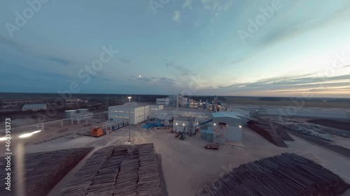 On a summer evening, a drone flight over a new modern woodworking plant - technological lines, pipelines, tall pipes, spacious workshops, conveyor lines, stored tree trunks