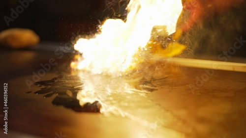 This slow motion video shows that hands of a hibachi chef setting a grill on fire to cook.