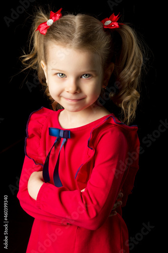 Cute blonde little girl standing on black backdrop