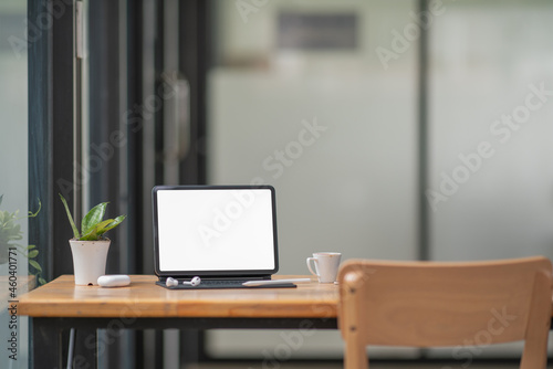 Blank screen tablet with keyboard and supplies on wooden table in co-workspace. © Songsak C