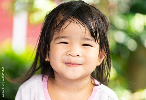 A headshot portrait of a cheerful baby Asian woman, a cute toddler little girl with adorable bangs hair, a child wearing a blue sweater smiling and looking to the camera.