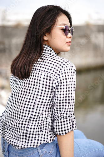 Young Beautiful Asian Woman Wearing Plaid Shirt And Blue Jeans Posing Outdoors