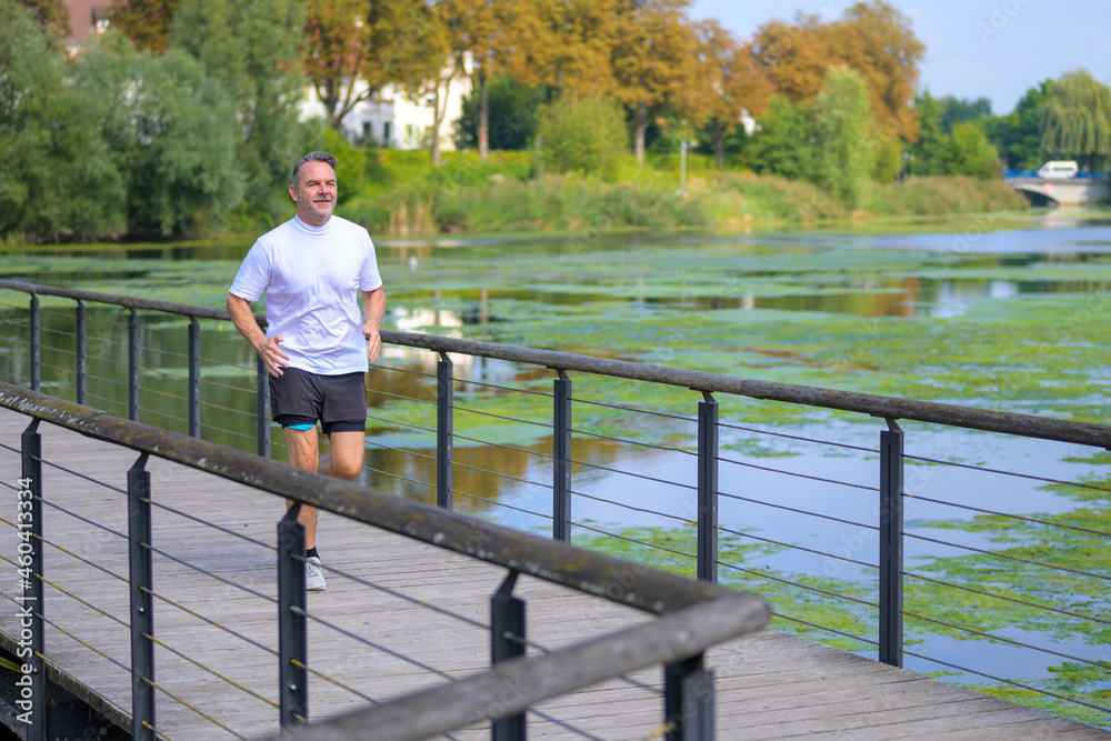Athletic man jogging across a bridge over a tranquil river