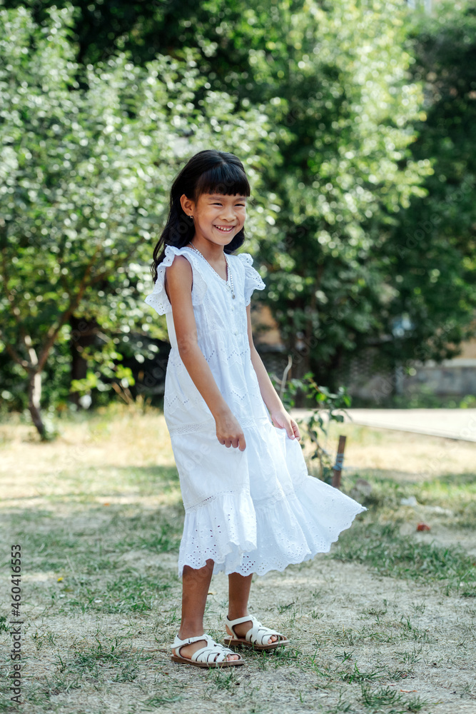 Cheeky little asian girl in white clothes standing on a grass in a park Cheeky little asian girl in white clothes standing on a grass in a park
