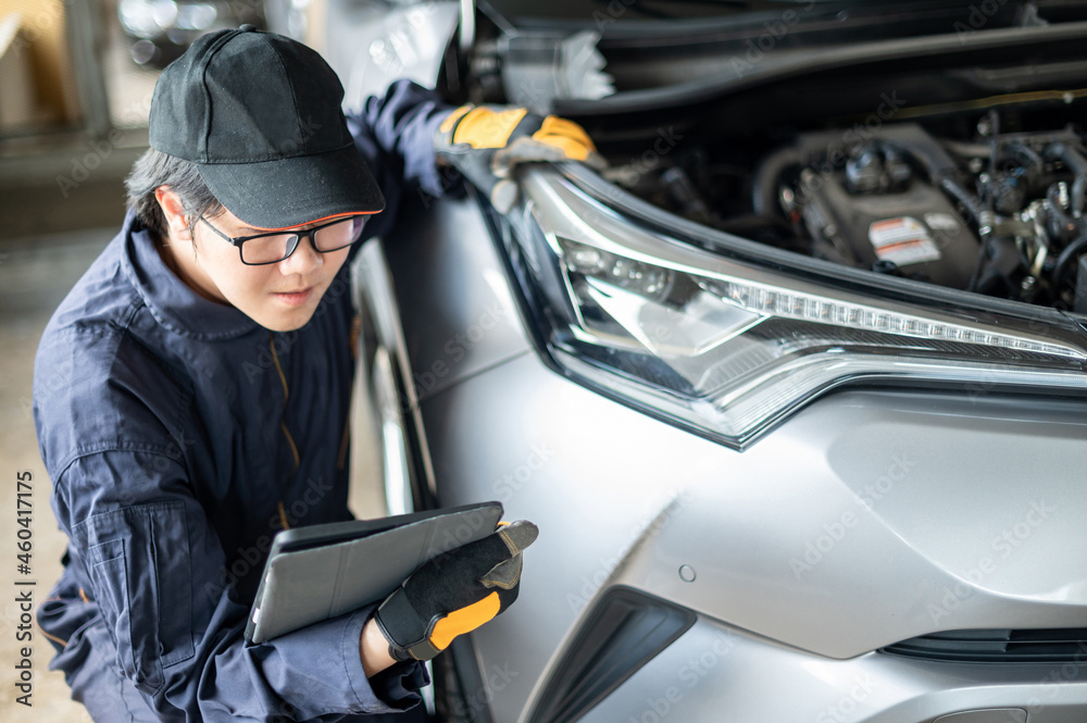 Asian auto mechanic holding digital tablet checking car wheel and tire in auto service garage. Mechanical maintenance engineer working in automotive industry. Automobile servicing and repair concept