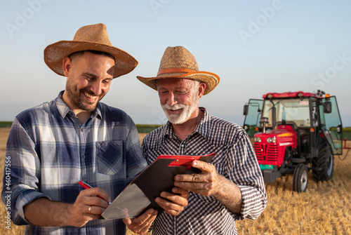 Quadro su tela Young farmer and senior agronomist signing documents in field with machinery in background
