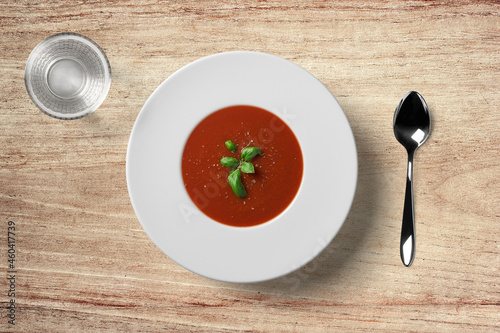Tomato soup in white plate with spoon and water glass on wooden background
