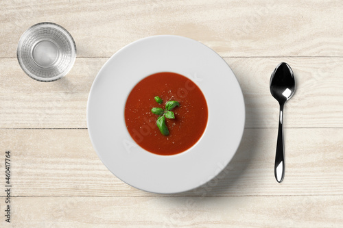 Tomato soup in white plate with spoon and water glass on wooden background