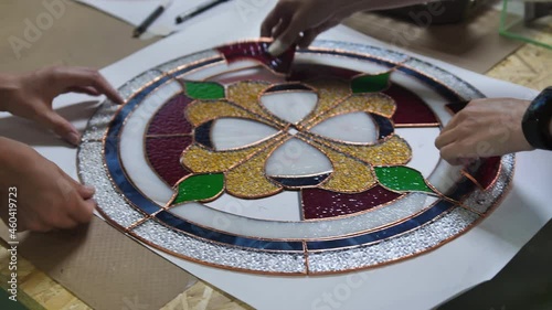 Two artists assemble a composition from stained glass windows. Assembling parts from a stained-glass window. Hands of two women. Craft, handmade. Tiffany stained glass. Details of the picture.