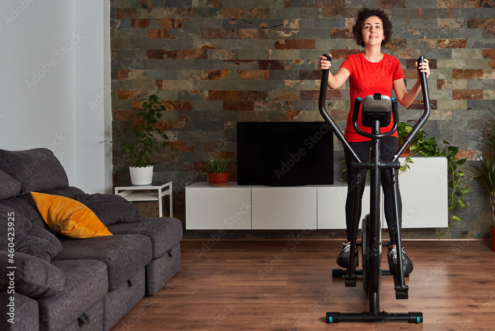 Woman training at home using elliptical cross trainer - obrazy, fototapety, plakaty 