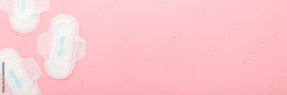 New opened white sanitary towels on light pink table background. Pastel color. Closeup. Wide banner. Female hygiene. Top down view. New opened white sanitary towels on light pink table background. Pastel color. Closeup. Wide banner. Female hygiene. Top down view.