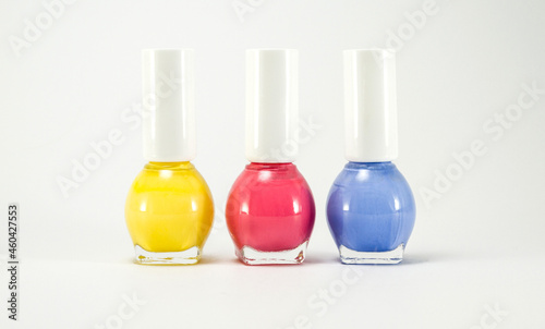 Three of glass bottles with colorful nail polishes on a white background. Assorted, various types of varnishes in yellow, pink and blue.