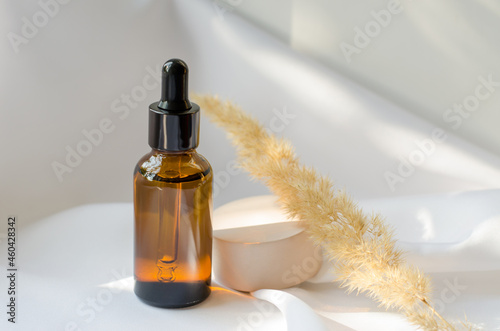 Essential oil or serum in a brown bottle with a dropper. A bottle of aromatic oil on a white silk cloth with pampas grass. Cosmetics, body care.