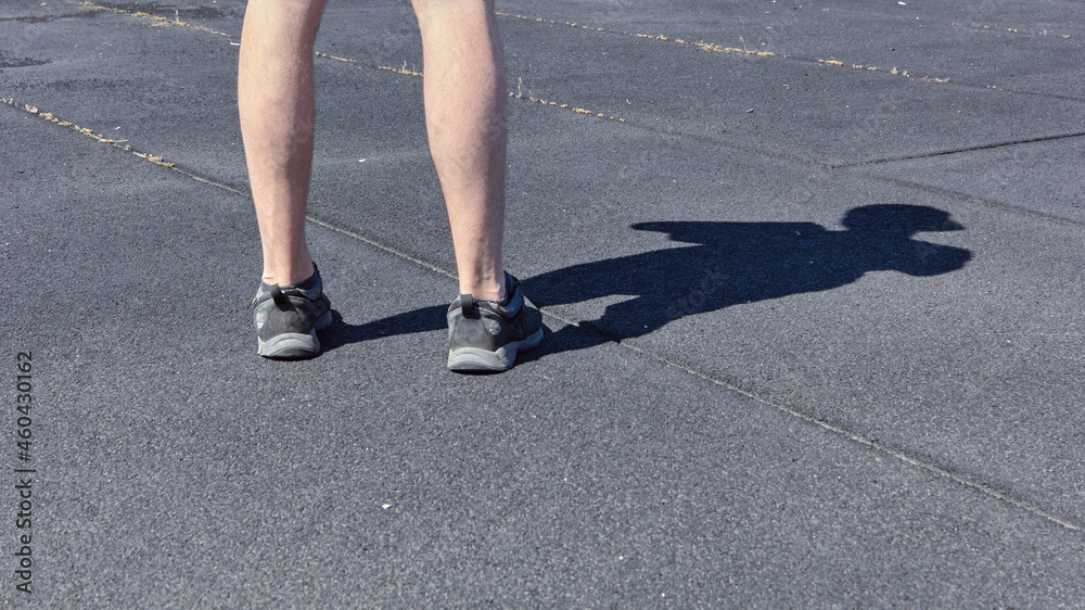 The legs of a man in short shorts and black sneakers. Black and gray asphalt background. The concept of running and walking. Legs of young man in black sneakers. 