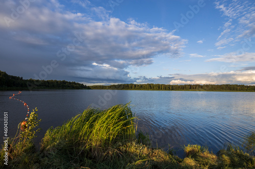 Cloudy sky over the river in the evening. Picturesque landscape with clouds and a river. Bright green grass in the foreground.