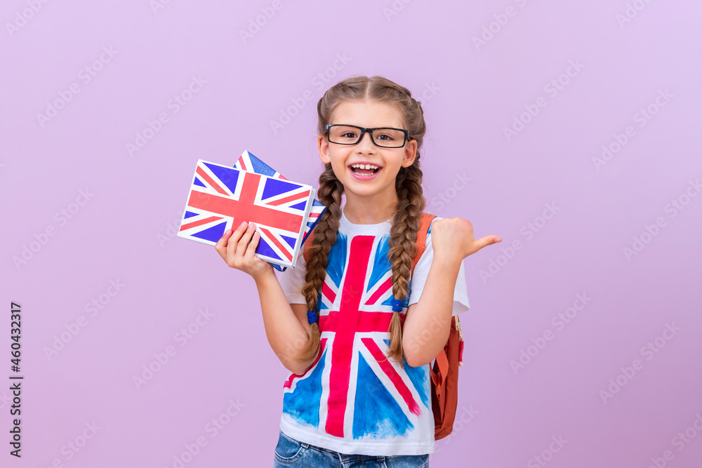 A child wearing glasses and a T-shirt with a British flag holds English books in his hand on a pink isolated background. A child wearing glasses and a T-shirt with a British flag holds English books in his hand on a pink isolated background.