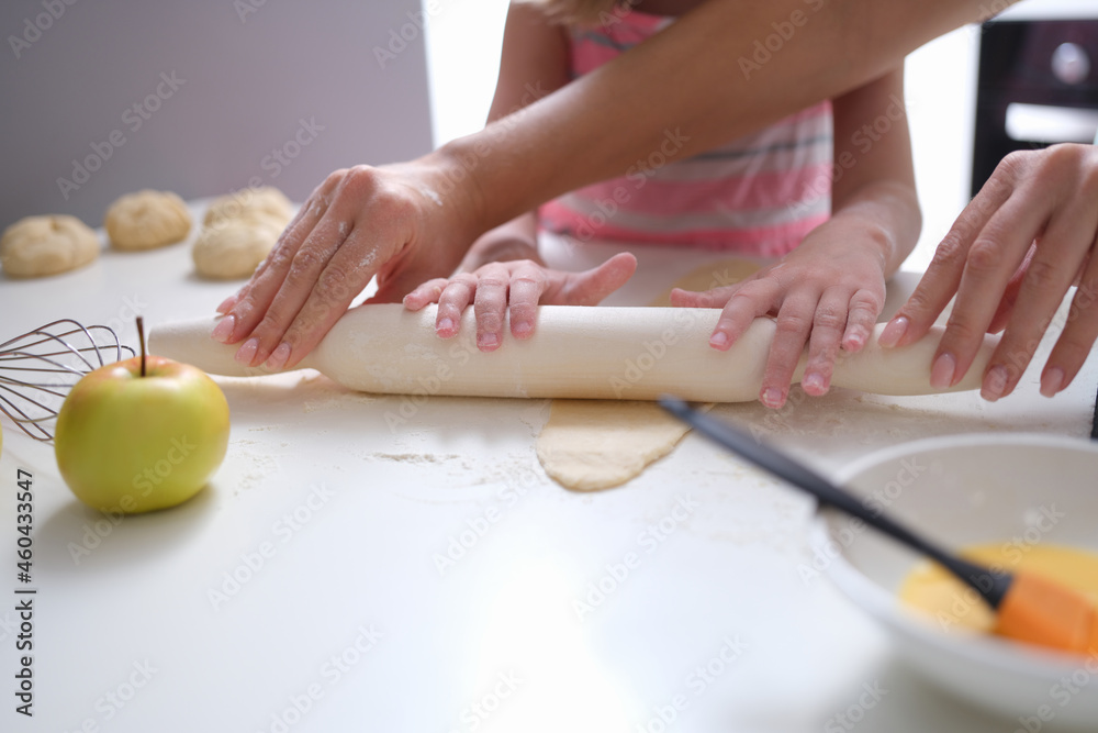 Mom and daughter roll out dough with rolling pin in kitchen Mom and daughter roll out dough with rolling pin in kitchen