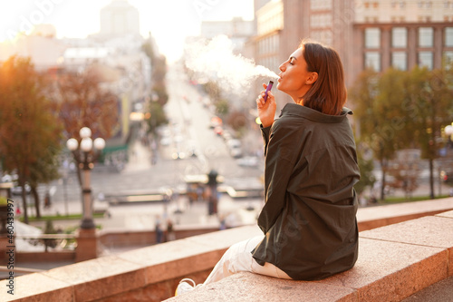 Woman at sunset with amazing city view, enjoying warm days, freedom, positive vibes, smoking  electronic cigarette photo