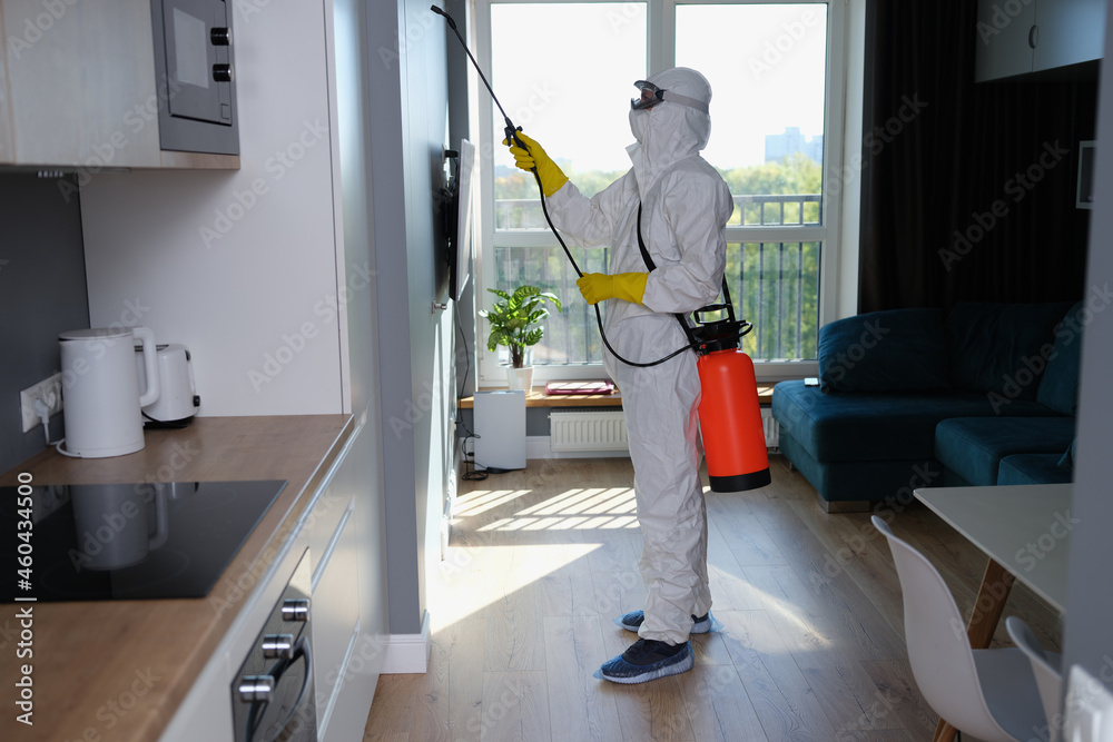 Person in white protective suit, mask and gloves with balloon disinfection in kitchen Person in white protective suit, mask and gloves with balloon disinfection in kitchen