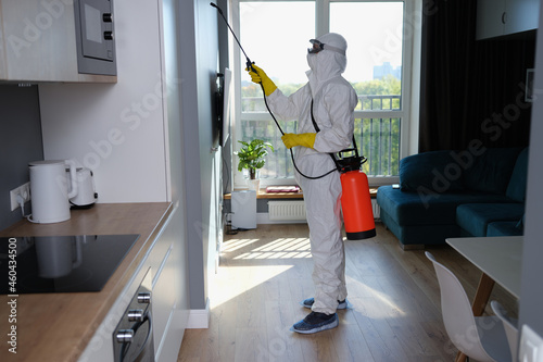 Person in white protective suit, mask and gloves with balloon disinfection in kitchen photo