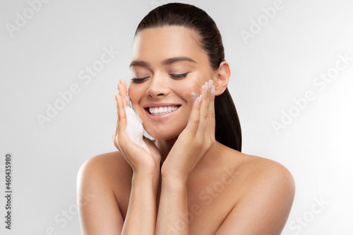 Happy woman with fresh perfect skin applying foaming cleanser for skincare and moisturizing at home. Young female with closed eyes and nude shoulders enjoy hydration procedure. Cosmetology concept