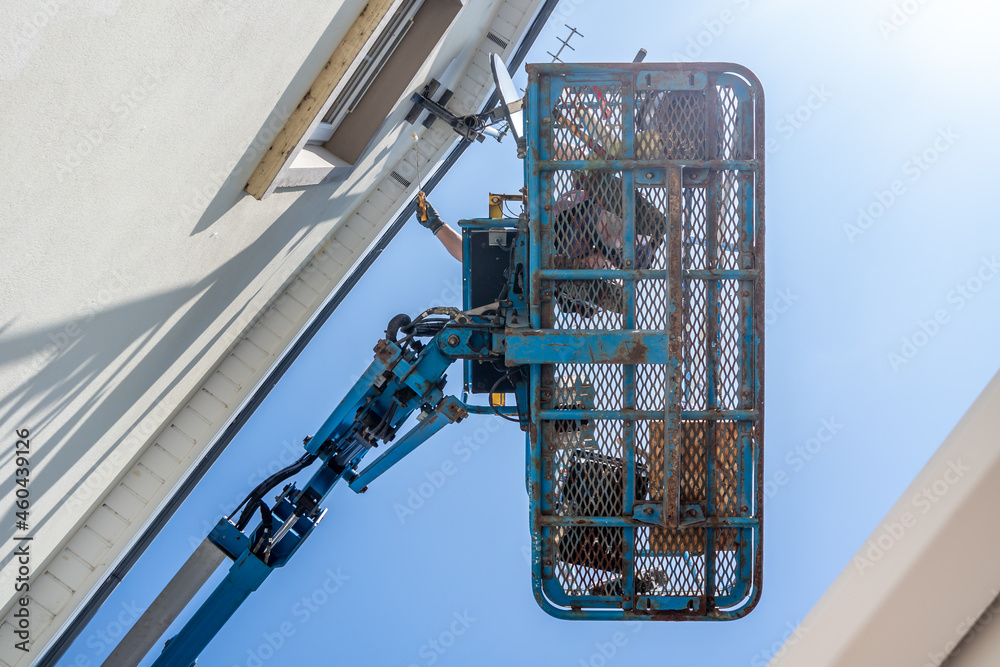 Fototapeta premium Worker on a aerial access platform, cherry picker, cleaning house