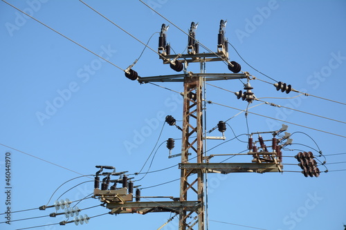 Low angle close-up view of the top part of an electricity distribution pylon and power lines under blue sky